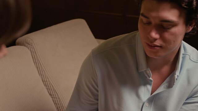 Tilt up shot of affectionate Caucasian man and woman touching each others hands while sitting on home sofa in evening