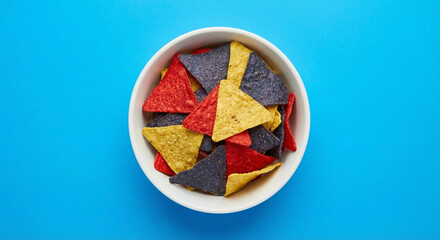 Colorful triangular tortilla chips in a white bowl on blue background.