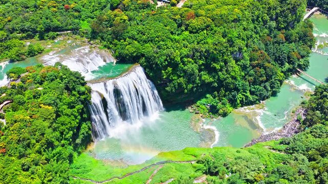 Aerial view of the famous Huangguoshu Waterfall cascading into a blue river surrounded by lush green forest in Guizhou, China.