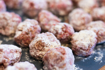 Raw meatballs coated in flour on a dark surface, ready for cooking