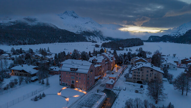 Aerial view of the village nestled amidst snow-covered landscapes and mountains under a soft twilight glow, Sils im Engadin/Segl, Grigioni, Switzerland.