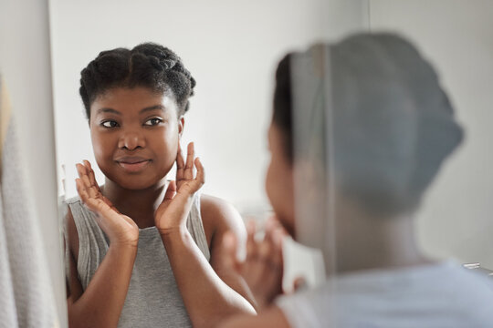 Smiling young African woman looking at her complexion in a bathroom mirror