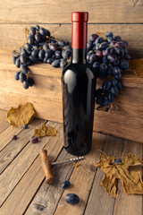 Obraz premium Bottle of red wine with blue grapes on a wooden table.