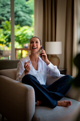 Fototapeta premium Happy brunette haired woman sitting in an armchair and using smartphone