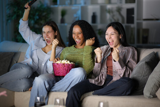 Excited diverse friends watching tv content at home in the night