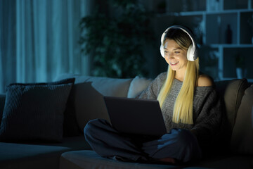 Happy woman in the night using laptop and headphone at home