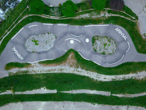 Aerial view of a pump track with 'ARINSAL' markings, nestled amidst green grass and trees, with winding paths, Arinsal, Andorra.