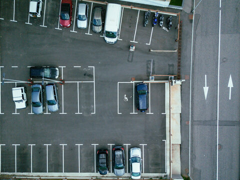 Aerial view of cars neatly aligned in a parking lot adjacent to a road marked with directional arrows, Arinsal, La Massana, Andorra.