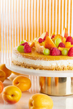 Cheesecake with fruit jelly on a marble table with apricots, against an orange background