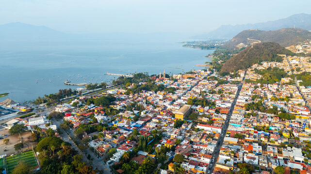 Aerial view of sun-drenched rooftops cascade towards the glistening lake framed by distant mountains, Chapala, Jalisco, Mexico.