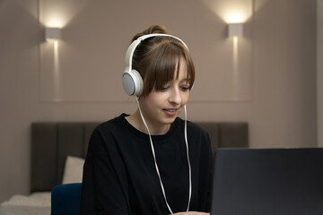 Focused young female freelancer wearing headphones working from home using laptop, enjoying comfortable and productive remote work environment