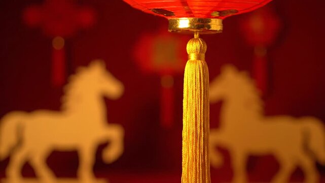 Red Chinese lanterns with golden tassels sway gently in the foreground. The background is a blurry, deep red canvas featuring illuminated white silhouettes of galloping horses, evoking a festive, tra