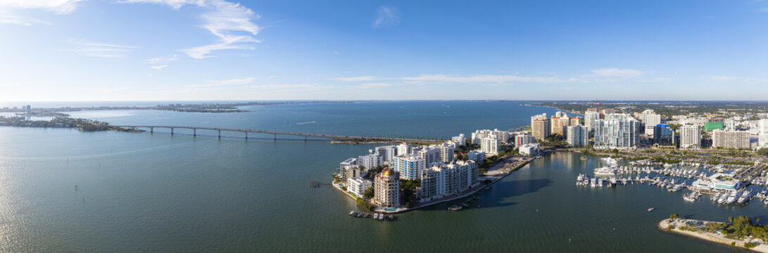 Aerial view of Sarasota's skyline meets the serene bay waters, Ringling Bridge stretches towards distant shores, and boats rest in the harbor, Sarasota, Florida, United States.