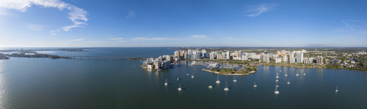 Aerial view of shimmering waters of Sarasota Bay dotted with sailboats lead to a vibrant cityscape of Sarasota with its modern buildings and Ringling Bridge, Sarasota, Florida, United States.