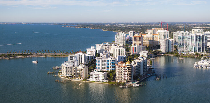 Aerial view of waterfront condos gleaming under the sun, contrasting with the deep blue waters and distant greenery, Sarasota, Florida, United States.