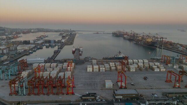 Aerial view of cranes and containers clustered densely in the harbor, reflecting the soft light of dawn over Cape Town, Western Cape, South Africa.