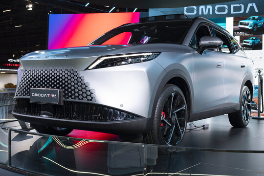 View of the Omoda 7 SUV, featuring a geometric grille, slim LED headlights, sporty wheels, and metallic finish at an auto show.