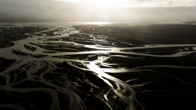 Aerial view of glacial rivers carve through the dark earth under a silver sky, creating an intricate web of light and shadow, Selfoss, Iceland.