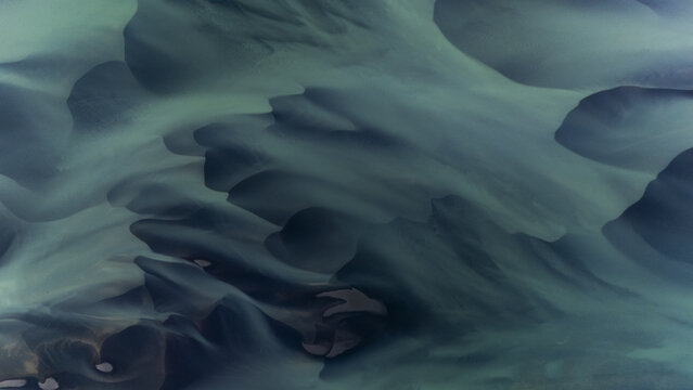 Aerial view of glacial rivers intertwine, carving paths through the stark, dark landscape, a dance of water and earth creating nature's masterpiece, Selfoss, Iceland.