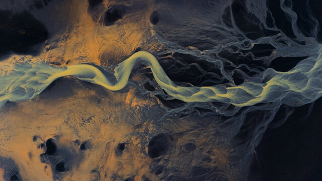 Aerial view of braided rivers carve paths through a landscape of contrasting gold and dark earth, creating a stunning natural tapestry, Selfoss, Iceland.