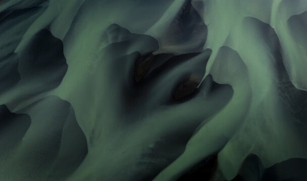 Aerial view of an ethereal dance of glacial rivers weaving through the stark Icelandic landscape, a symphony of muted greens and deep shadows, Selfoss, Iceland.