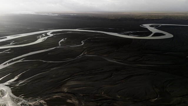 Aerial view of glacial rivers carve intricate paths through the dark, volcanic plains, a stark contrast under the Icelandic sky, Selfoss, Iceland.
