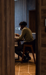 Businessman working remotely on laptop while sitting at table in hotel room.