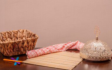 Traditional tabletop still life featuring wicker basket, bamboo mat, decorative metal food cover and kitchen cloth. Representing home dining, cultural simplicity and rustic lifestyle concept.