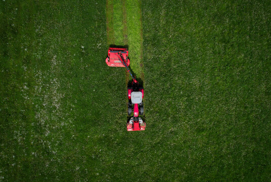 Aerial view of a red lawn mower leaving trails on the lush green grass, Chavannaz, Auvergne-Rhone-Alpes, France.