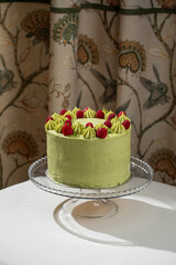 Elegant pistachio raspberry cake with smooth green cream and fresh berries presented on a glass stand