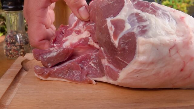 A chef hand places a fresh raw leg of lamb on a wooden table. The red meat is ready for seasoning and roasting. Perfect for culinary videos and meat preparation concepts in the kitche