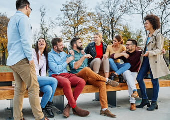 Fototapeta premium Group of young happy people or students having fun together outdoors in street or park or outside the university college or school. Happy friendship concept with young people having fun together. Youn