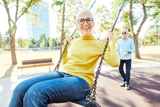 Happy active senior couple having fun on a swing in park outdoors