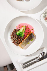 Grilled salmon fillet served with quinoa broccoli and pink sauce on white plate