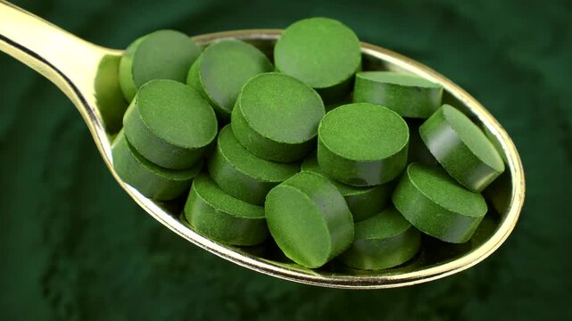 Chlorella or spirulina algae green powder pills in spoon with circle rotation. Dietary supplement to improve health. Seaweed superfood. Healthy food background. Vitamins and minerals to diet detox
