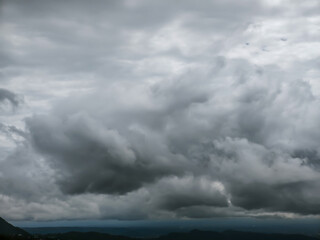 Obraz premium Dense grey storm clouds swirl across a dark, moody sky over a faint mountain horizon. This dramatic atmospheric scene captures the raw power of nature before a heavy rain in the highlands.