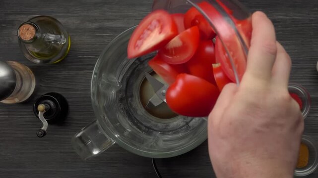 Top down view. Sliced fresh red tomatoes are poured into a blender bowl to make a healthy sauce, soup, or smoothie. Food preparation in the kitchen
