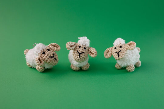 Three cute handmade crochet sheep toys on green background. Amigurumi farm animals for nursery decor, knitting hobby shop, eco toys business and DIY craft projects. Soft wool texture