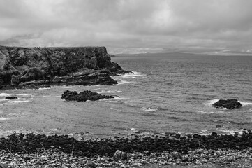 A black and white photo of a rocky shoreline with a large body of water in the b
