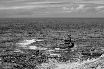 A rocky shoreline with a small rock in the middle of the ocean