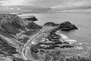 A black and white photo of a rocky shoreline with a road running along it