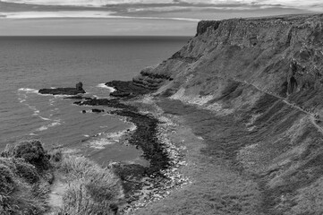 A black and white photo of a rocky shoreline with a cliff in the background