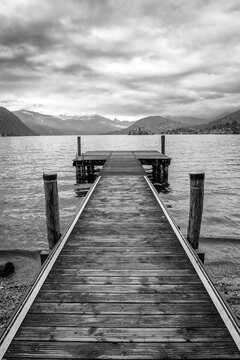 Wooden jetty along the winter water of Orta Lake (piedmont, Northern Italy) with the alps in the background. UNESCO World Heritage Site, its San Giulio island is home to a convent of cloistered nuns.