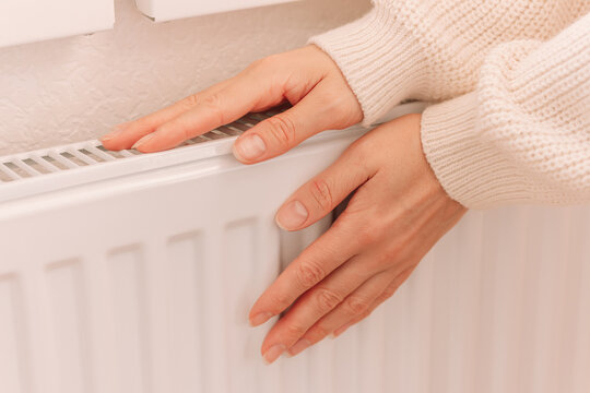 Woman's hands warming near a radiator on a cold winter day.	