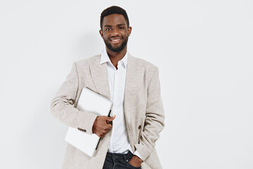 Confident smiling man holding laptop and notebook, dressed in beige blazer and white shirt,...
