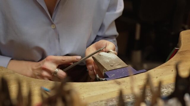 Professional jeweler filing silver ring on workbench.