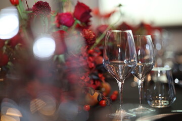 Empty crystal wine glasses reflecting light on dark table, featuring a beautiful red floral centerpiece creating an atmosphere for celebration, fine dining, and luxury events