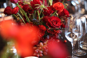 Elegant table setting showcasing rich red floral centerpiece with roses and ranunculus, complemented by grapes and empty wine glasses, creating an atmosphere of celebration and romance for events