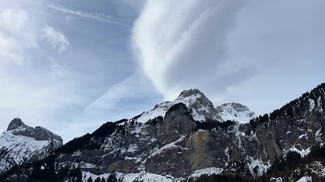Fast-moving clouds above high and rocky mountains. Time-lapse of the Swiss Alpine landscape on a cold winter day. Snowy mountain peak against a cloudy sky. Kandersteg, Berner Oberland, Switzerland.