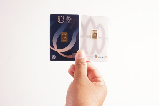 a man is holding 1 gram from antam gold and 3 gram from ubs gold on a isolated white background                        
